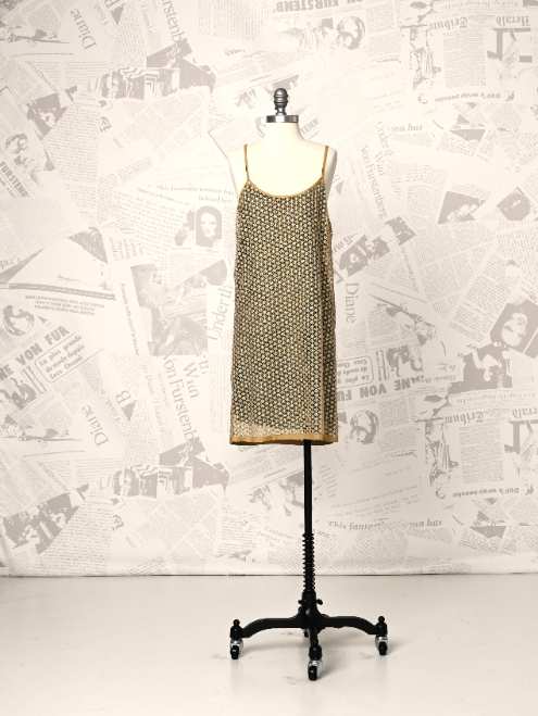 Mannequin wearing a patterned dress against a newspaper-textured wall.