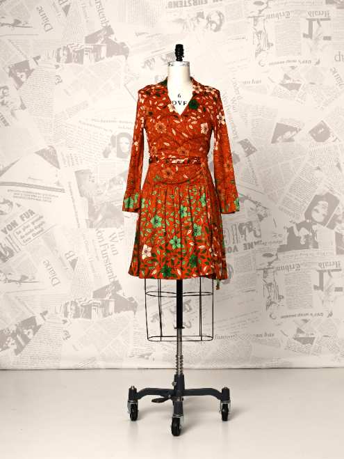 Orange floral dress on a mannequin against a newspaper-patterned wall.