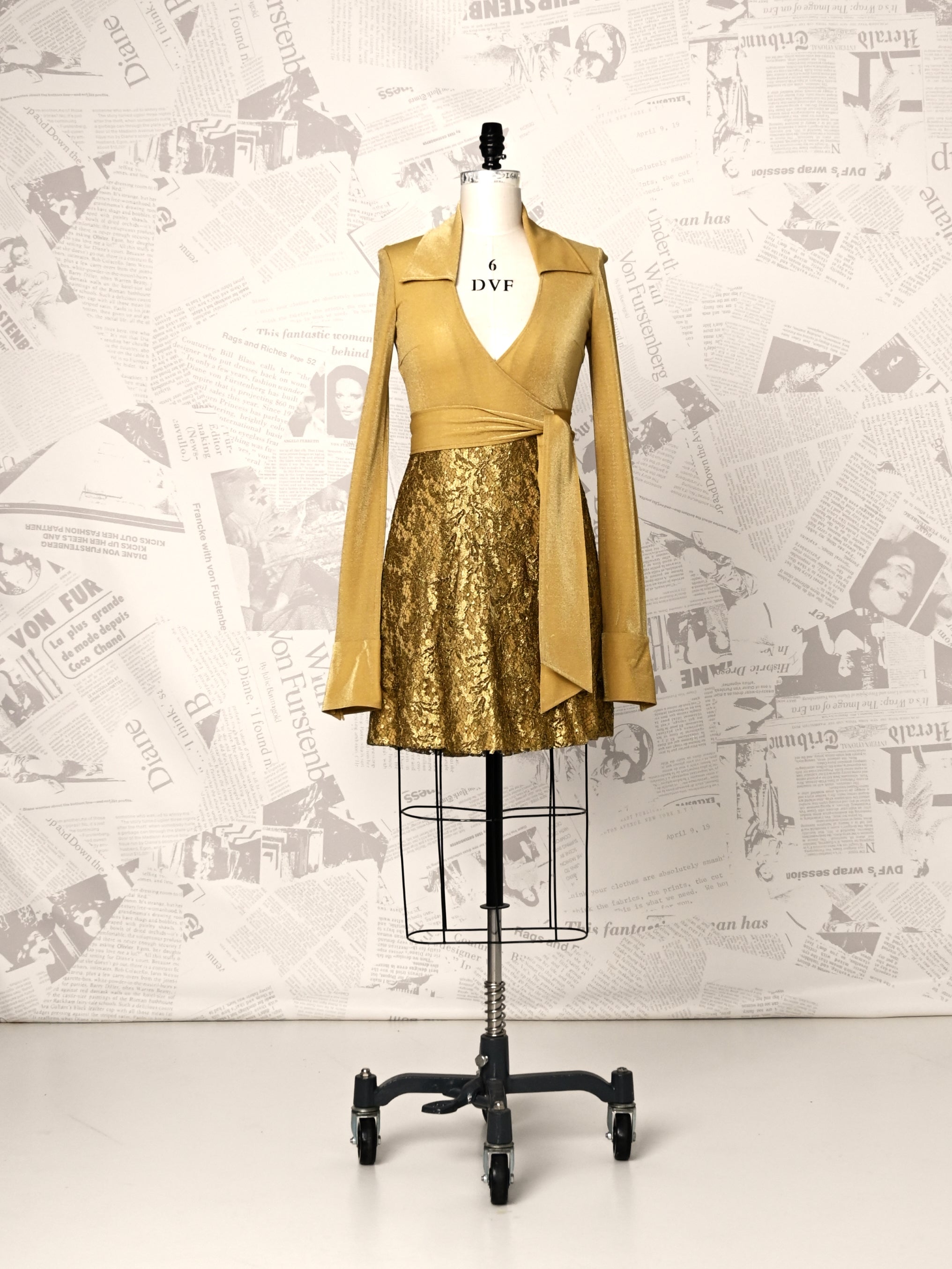 Mannequin wearing a gold outfit with a sequined skirt against a newspaper-patterned wall.