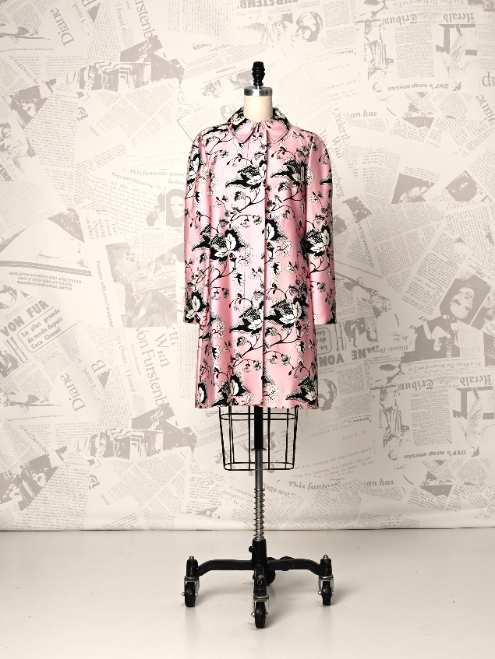 Pink floral dress on a mannequin against a newspaper-patterned wall.