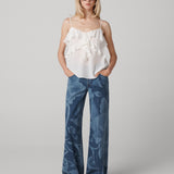 A woman wearing a white sleeveless top with ruffled neckline and blue denim pants with a floral print